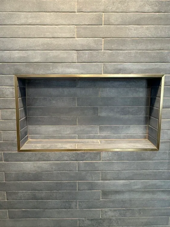 Close view of a horizontal recessed shower niche framed with warm metallic trim in charcoal gray rectangular tile.