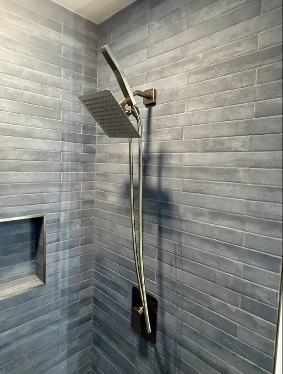 Charcoal gray tiled shower corner with a warm-metal hand shower, square rain-style head, and trimmed recessed niche.