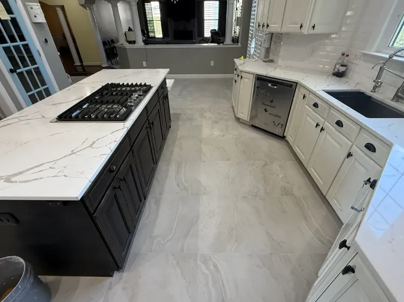 Gray veined tile floor viewed from a black kitchen island toward white cabinets, a sink, and a blue glass-paneled door.