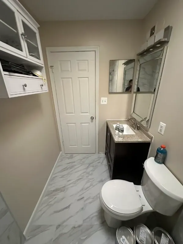 Narrow bathroom view with a dark vanity, white toilet, chrome fixtures, and gray-veined marble-look floor tile.