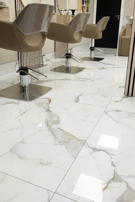 Row of taupe styling chairs above large glossy white floor units with flowing gray veining.