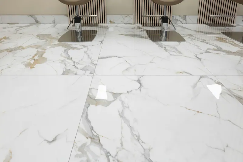 Low view across glossy white veined floor units beneath styling-chair bases and striped wall panels.