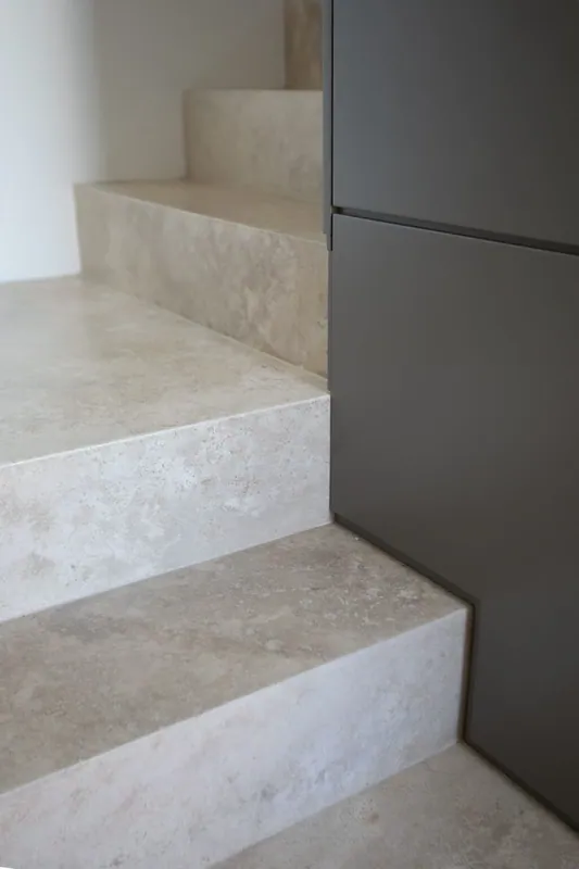 Close view of light beige veined tile on a stair landing beside a gray cabinet and wood trim.