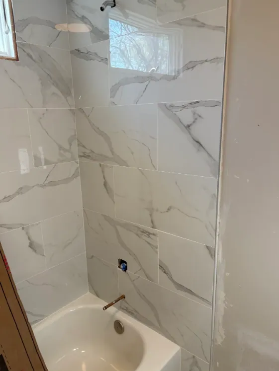 Tub-and-shower surround with broad gray-veined white wall tile and a high window.