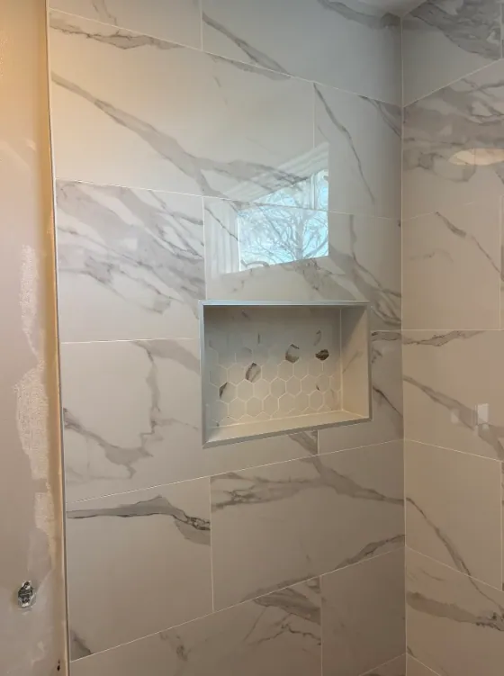 Recessed shower niche with small hexagonal accent tile framed by broad gray-veined wall tile.